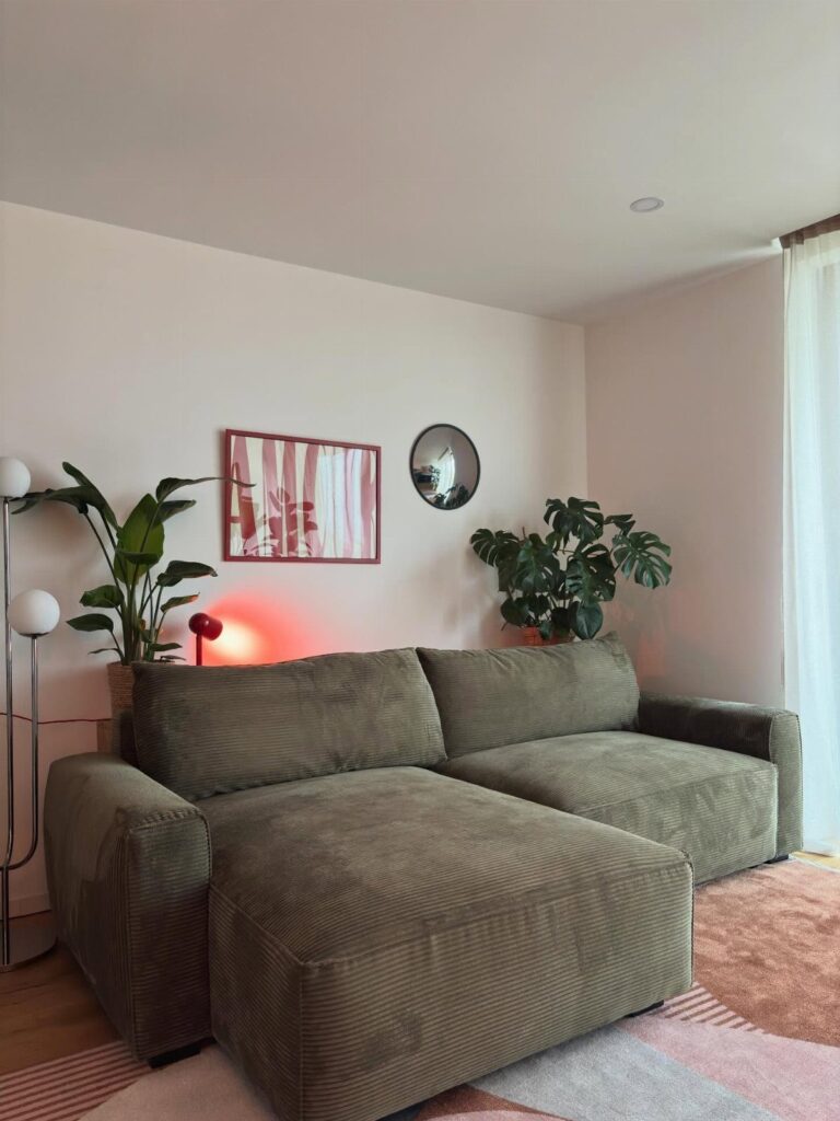 Green corduroy sectional sofa with abstract art and plants on a pink wall