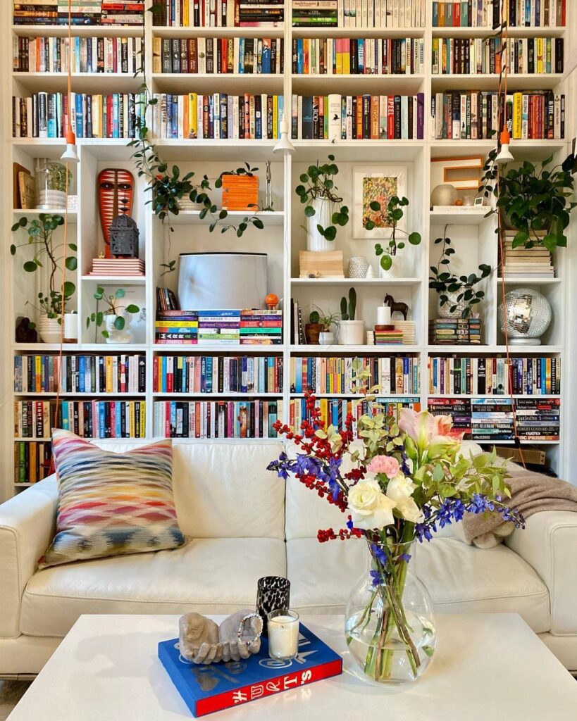White floor-to-ceiling bookshelves filled with books and plants behind a white living room sofa.