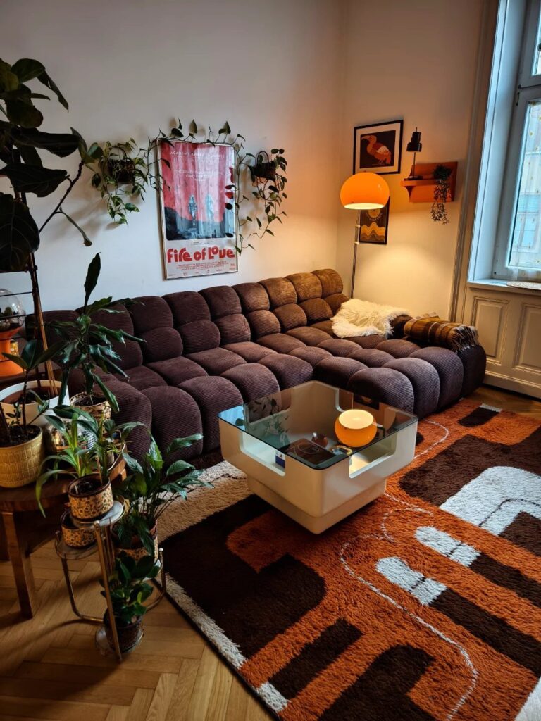 Brown tufted modular couch in a living room with plants and orange rug