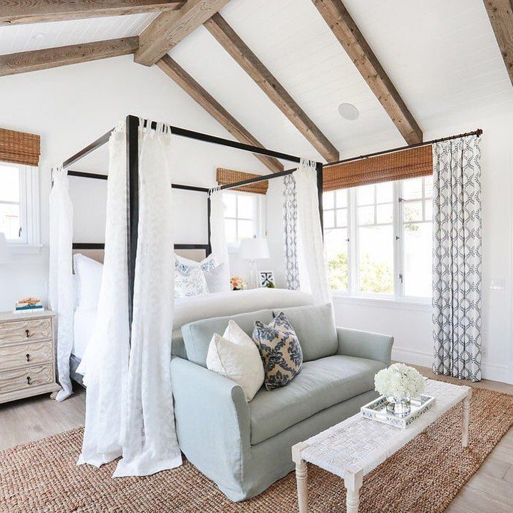 Light blue couch positioned in front of a black four-poster bed in a bedroom.