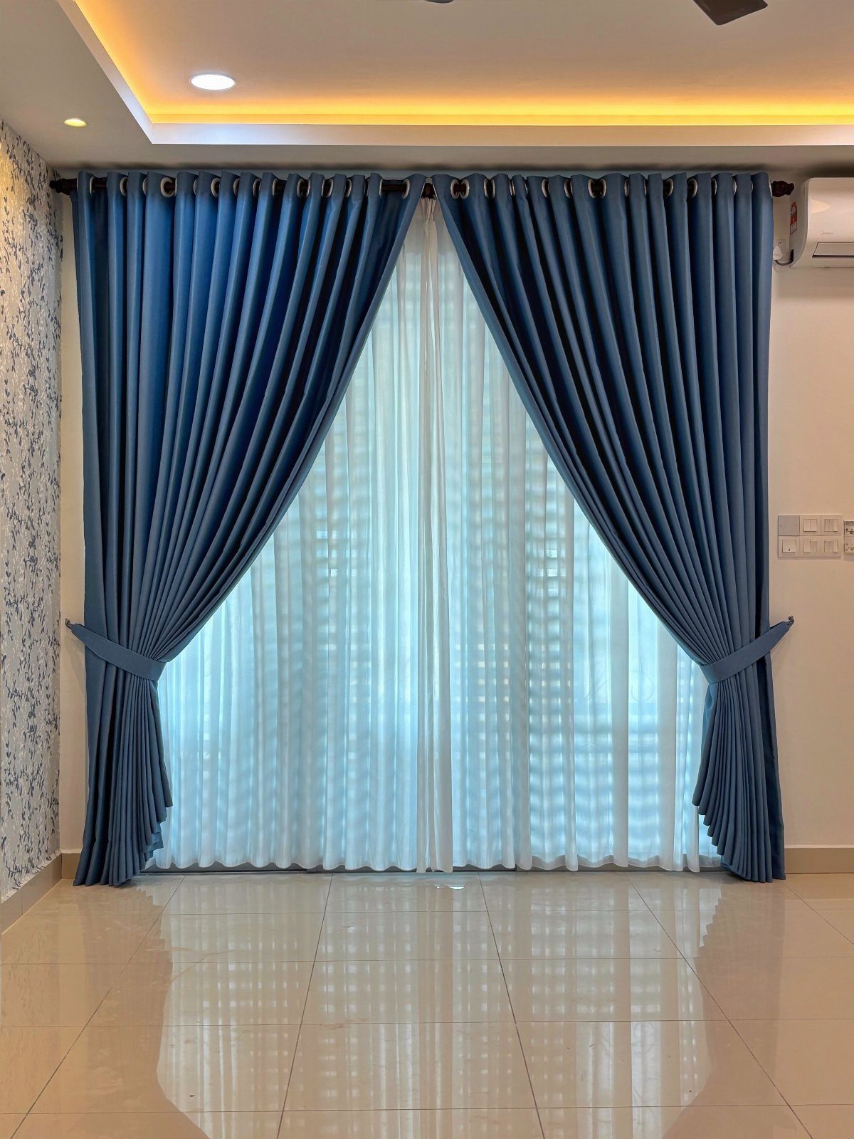 Blue draped curtains with tie-backs and sheer white under-curtains in a living room.