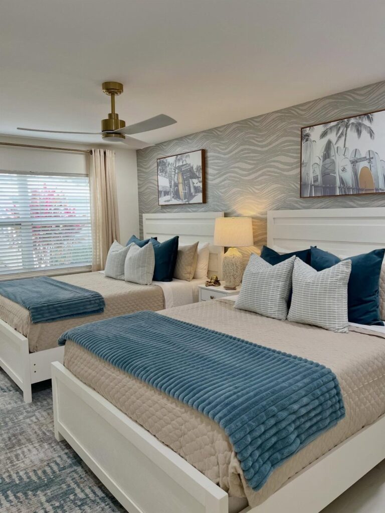 Two white beds with blue and beige bedding in a coastal themed bedroom.