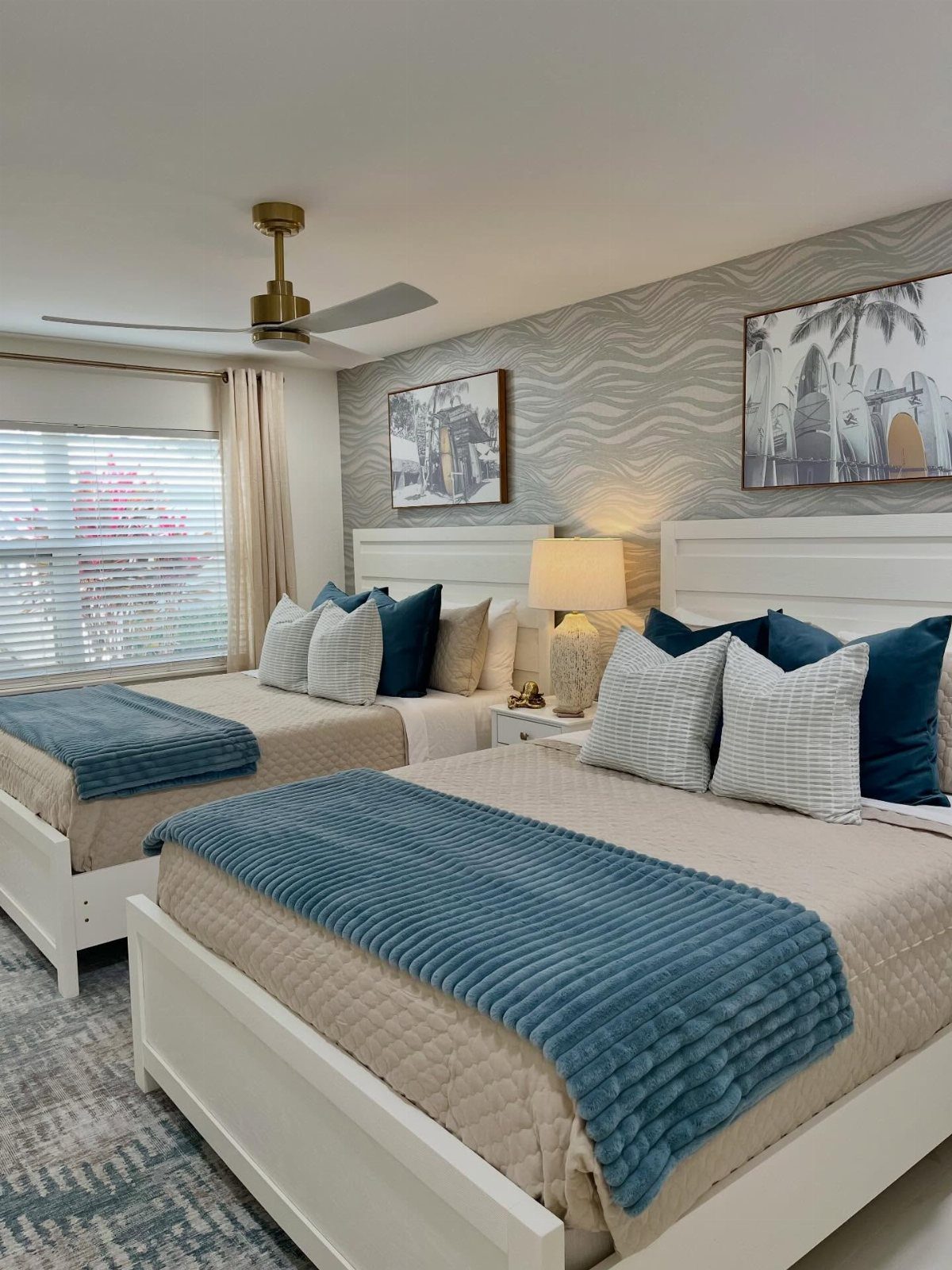 Two white beds with blue and beige bedding in a coastal themed bedroom.