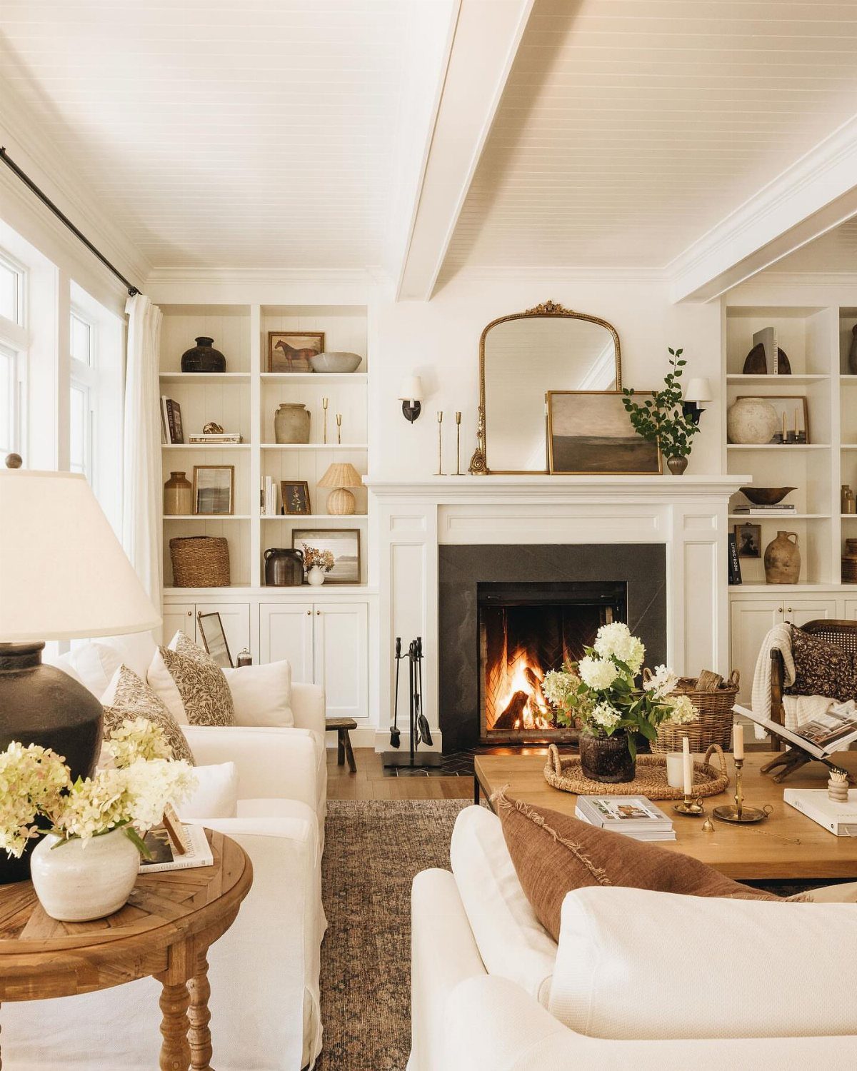 Living room with white sofas arranged around a burning fireplace and built-in bookshelves.