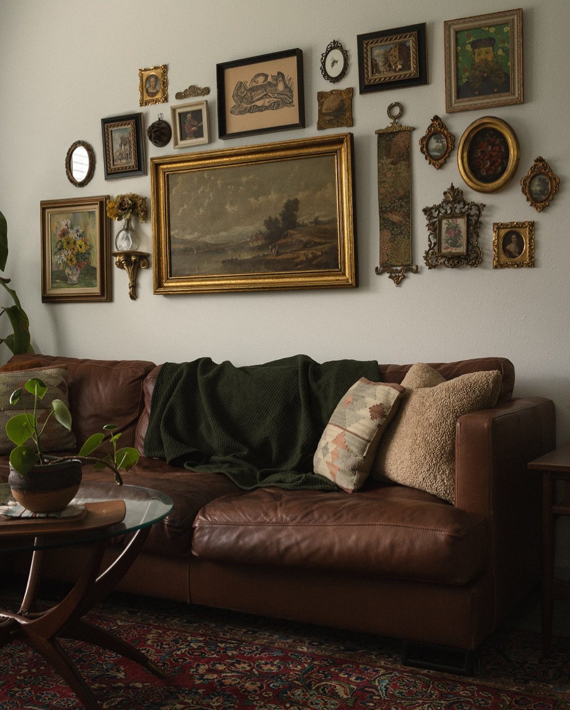 Brown leather sofa beneath a gallery wall of eclectic framed art and mirrors.