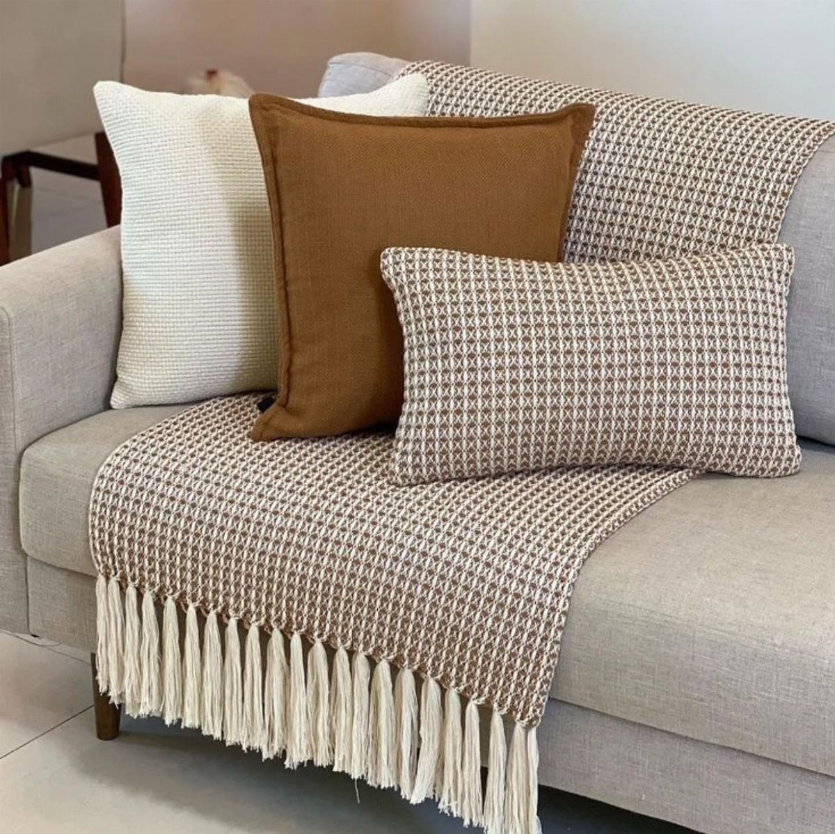 Patterned brown and white throw blanket with tassels styled on a grey sofa