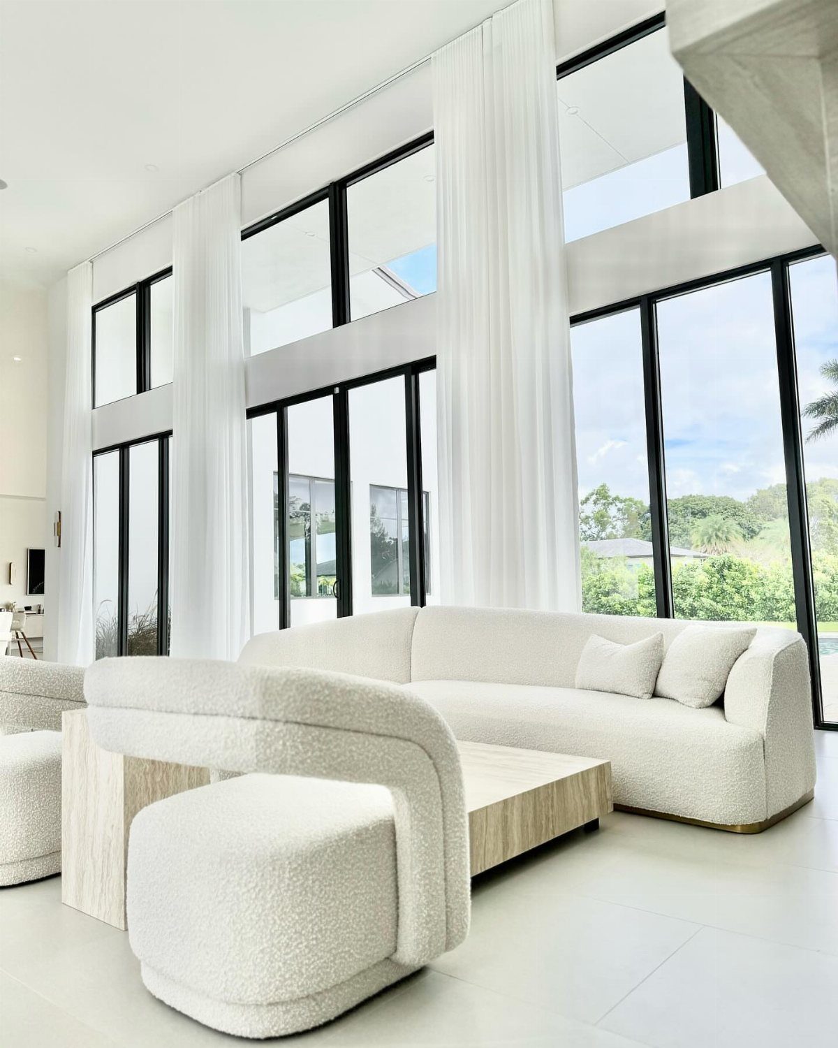 White drapery panels framing large black windows in a modern white living room