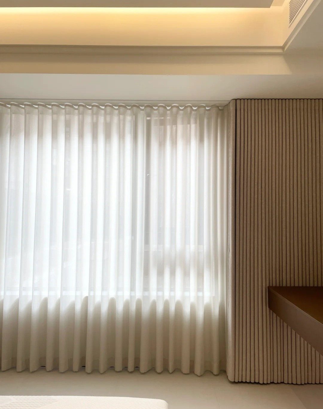 White sheer curtains hanging in a modern room next to a slatted wall.