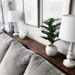 Grey couch with a narrow wooden shelf between the backrest and white wall.
