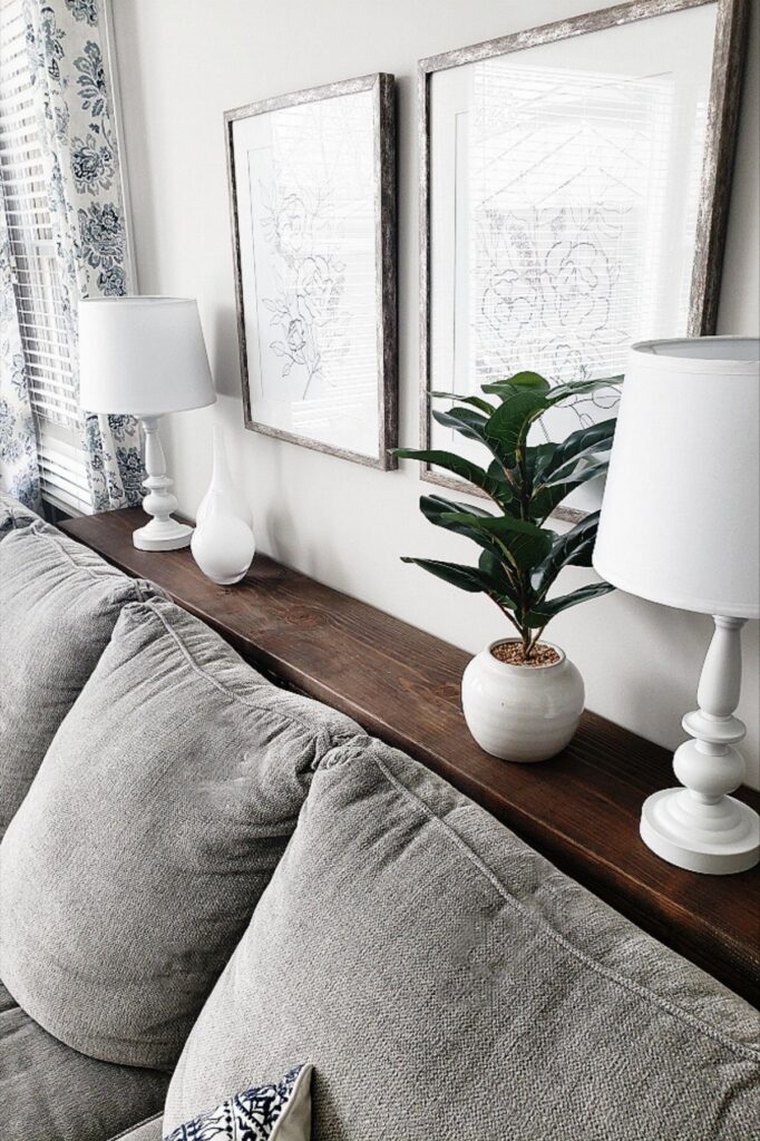 Grey couch with a narrow wooden shelf between the backrest and white wall.